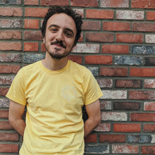 Load image into Gallery viewer, There is a picture of a male model standing in front of a brick wall wearing the yellow version of the shirt.